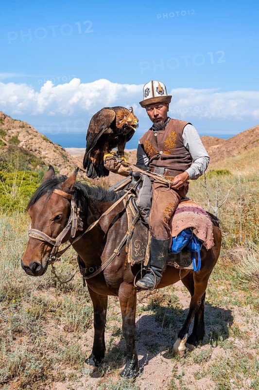 Traditional Kyrgyz eagle hunter with eagle in the mountains, hunting on horseback, near Kysyl-Suu, Kyrgyzstan