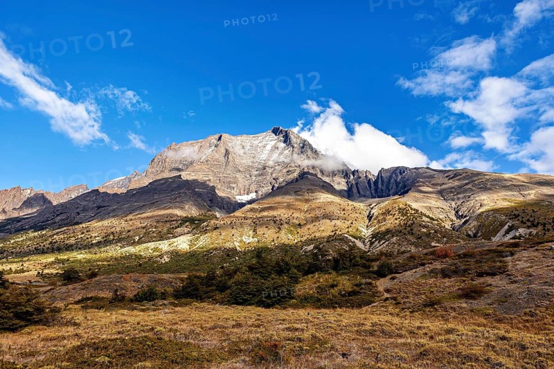 High mountain with hidden peak under blue sky and clouds, surrounded by green meadows, The landscape of the Torres del Paine National Park in Patagonia Chile