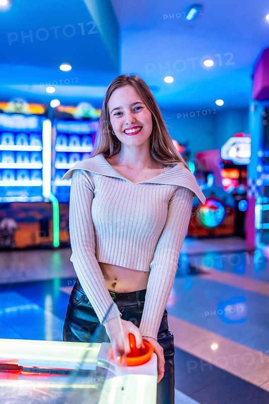 Smiling young woman enjoying a game of air hockey in a vibrant, colorful entertainment center filled with neon lights and excitement