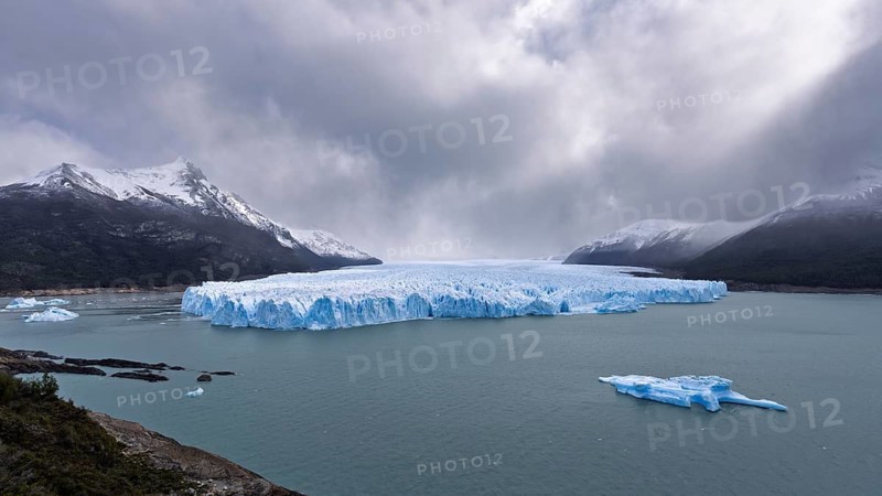 Perito Moreno glacier with blue ice front, floating ice floes in Lake Argentino, snow-capped mountains and cloudy sky in the background, Los Glaciares National Park, Santa Cruz Province, Patagonia, Argentina