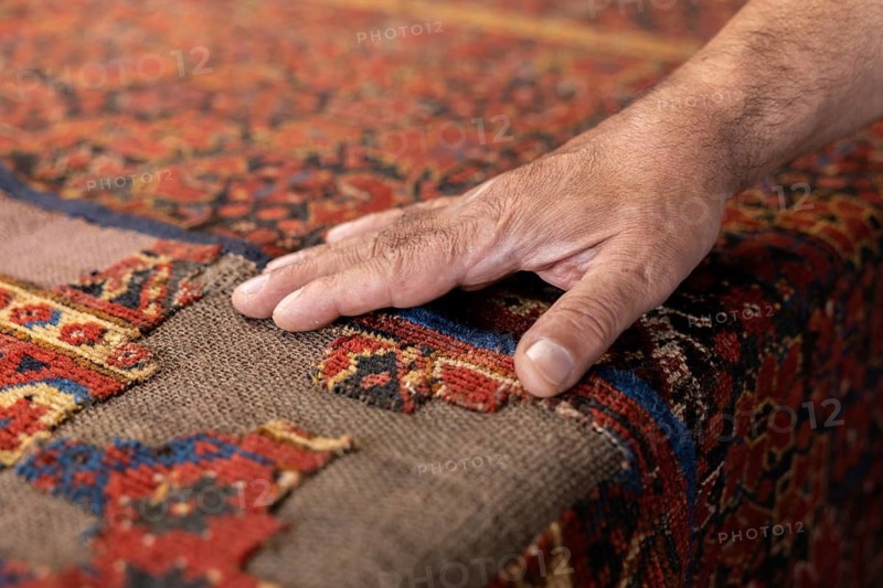 Cropped unrecognizable Iranian carpet restorer works diligently in his Salzburg workshop, demonstrating a rare skill as he meticulously repairs an old, vibrant carpet
