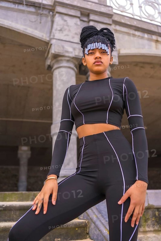 Black ethnic girl with braids with with black full body suit. Posé on some stairs next to the beach