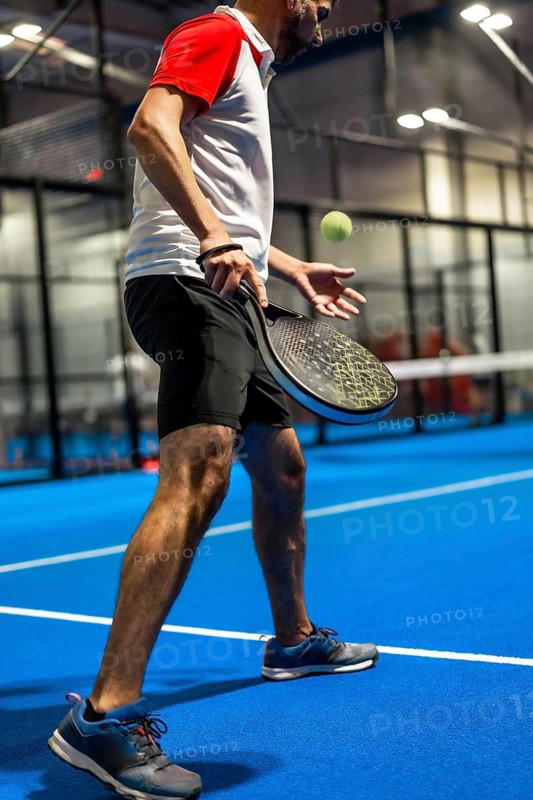 Vertical photo of a mature caucasian man serving while playing paddle tennis with friends