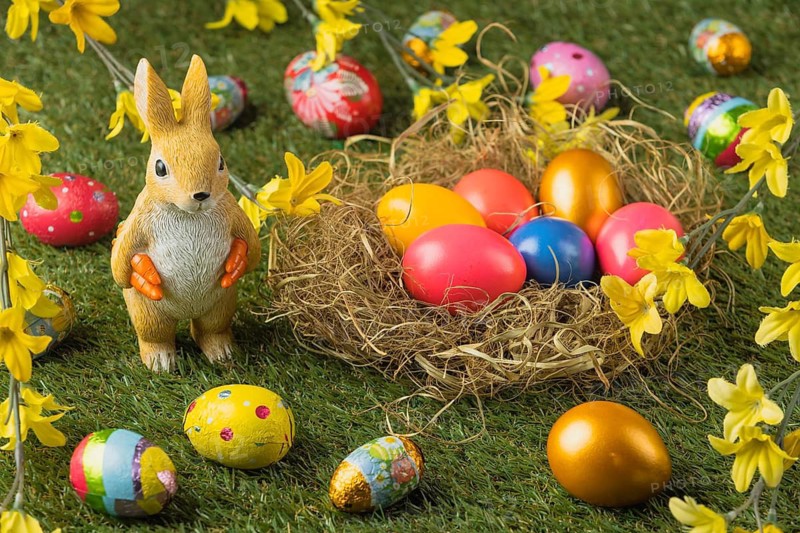 A rabbit figure stands next to a nest full of colorful Easter eggs, decorated with yellow flowers