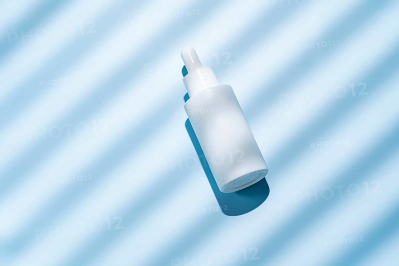 Top view of a white cosmetics bottle on a serene blue, striped background, illuminated by soft sunlight creating gentle shadows. Ideal for clean beauty themes