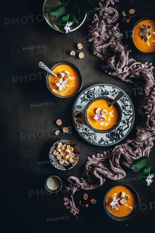 Elegant overhead image showcasing creamy autumn soup garnished with croutons and flowers. Displayed in ornate bowls with a rustic cloth, creating a cozy dining atmosphere
