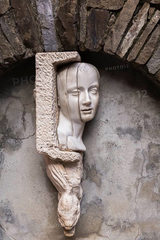 Close-up of white sculpted head and serpent on water fountain and arch made of old stones, Manarola, Cinque Terre, La Spezia province, Italy