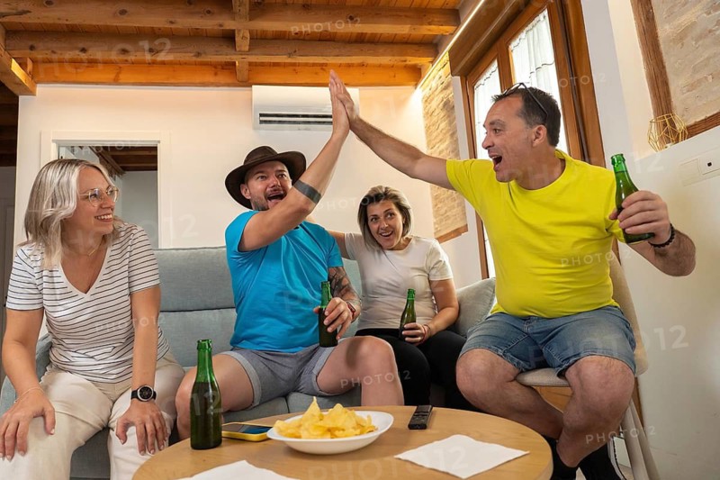 Group of friends celebrating a goal while watching a soccer match on TV at home. Excited emotions, cheering, friendship, leisure time and sports entertainment indoors