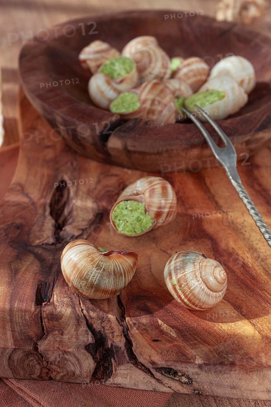 Snails cooked with herb oil on a wooden plate, served with white wine, natural light, no people