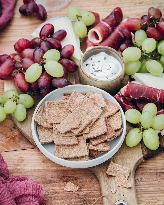 An inviting snack platter featuring crisp crackers, juicy grapes, cured meats, and a creamy dip. Perfect for a social gathering or casual appetizer