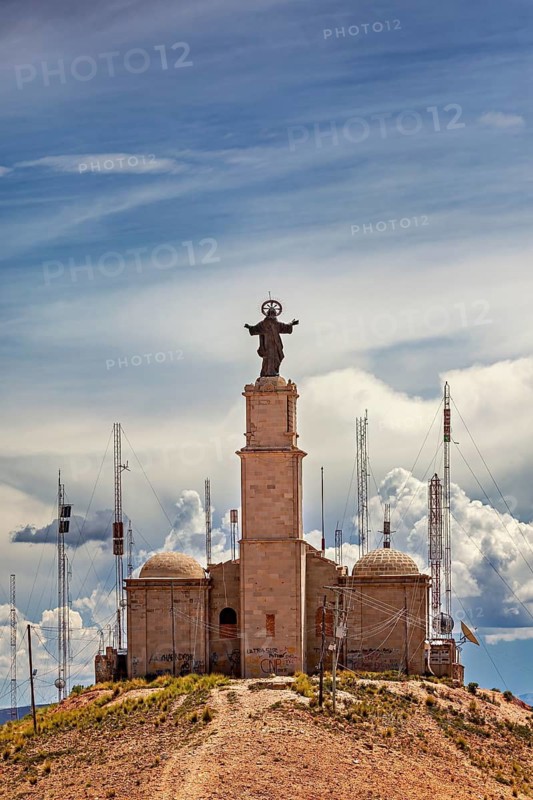 A church with a statue on it, surrounded by antennas, stands on a hill under a cloudy sky, The church on the mountain of silver mines near Potosi on Cerro Rico in Bolivia