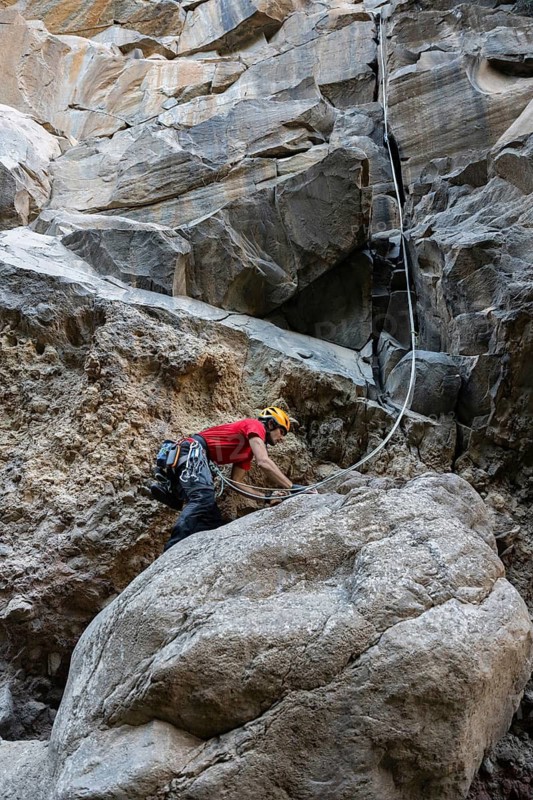 A climber in a red shirt tackles a challenging rocky cliff using traditional climbing techniques. The rugged terrain offers an exhilarating experience surrounded by nature