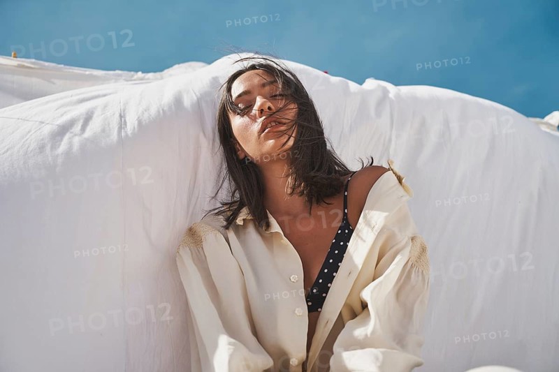 A woman enjoys a sunny summer day on the rooftop, wearing a casual shirt over a swimsuit Her serene expression captures the essence of relaxation and leisure
