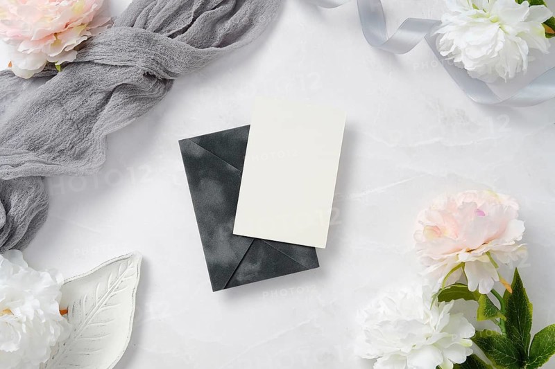 Elegant wedding stationery set on marble, featuring a dark envelope and white card. Adorned with delicate flowers, ribbon, and lace, creating a sophisticated wedding theme