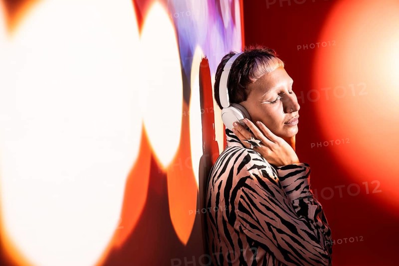 A young, trendy woman wearing oversized headphones enjoying music. She stands against a colorful backdrop, embodying a modern and artistic lifestyle