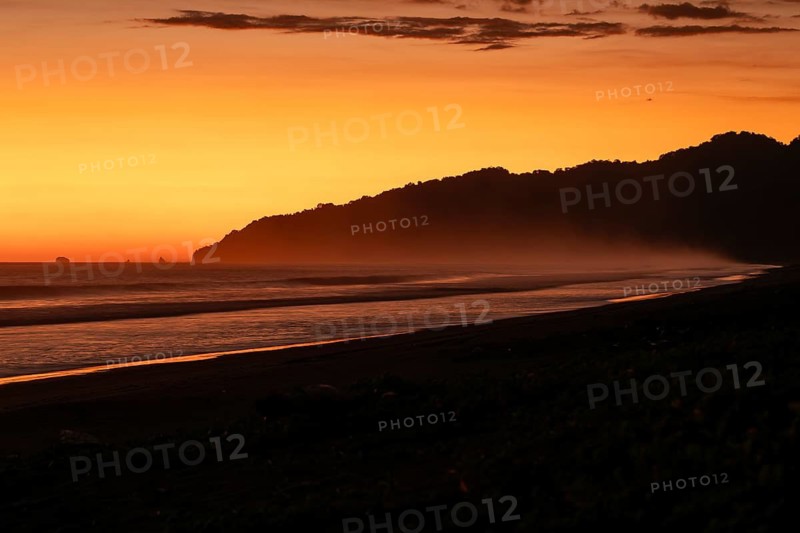 After sunset, the deep red sky glows above palms and ocean spray with views of Corcovado National Park. Costa Rica