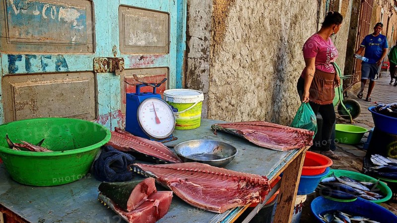A table with huge fish fillets of tuna (thunnus) and a scale on a market stall with people in the background, Mindelo fish market, Mindelo, Sao Vicente, Cabo Verde, Cape Verde, Cape Verde