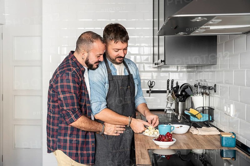 A loving gay couple sharing a joyful moment while preparing a meal in a modern kitchen. They are smiling, surrounded by fresh produce on a neat countertop