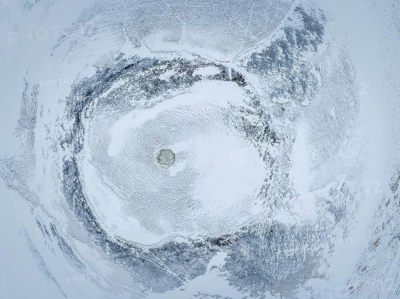 Discover the mesmerizing patterns of a snow-covered landscape from above. This aerial shot captures the serene beauty and intricate textures of Iceland's frozen terrain