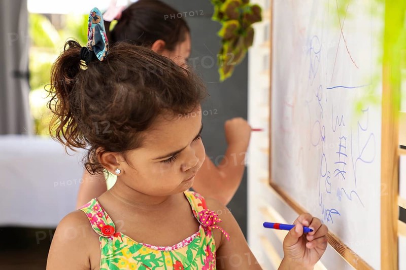 Young children enjoy drawing on a whiteboard at home, highlighting creativity and family bonding. The colorful scene captures the essence of joyful learning
