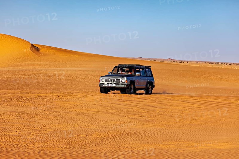An off-road vehicle drives through vast sand dunes in a sunny desert landscape, off-road through the Sahara in Algeria