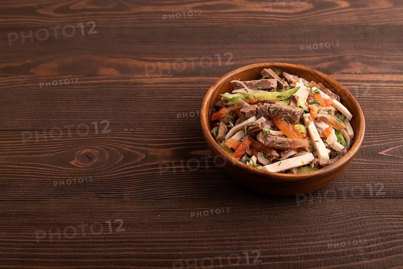 Meat salad with beef and vegetables in wooden bowl on brown wooden background. side view, copy space