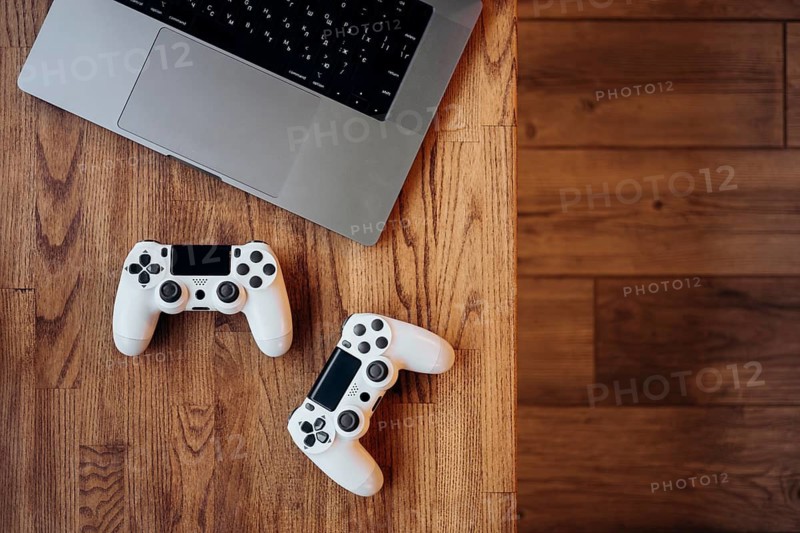 A gaming setup featuring a laptop and two white controllers on a wooden desk. The image captures the blend of modern technology and classic design, ideal for gaming enthusiasts