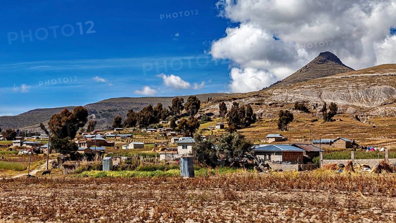 Small village in a hilly landscape with a mountain backdrop and a blue sky, The villages and countryside near Puno in Peru