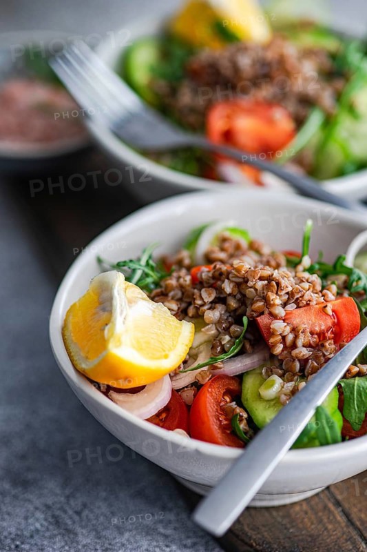 A vibrant healthy lunch made with fresh rocket, chopped oregano, cherry tomatoes, cucumber, red onion, steamed buckwheat, lemon, Himalayan salt, and organic olive oil