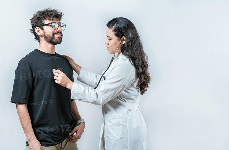 Asian doctor checking a patient heartbeat with a stethoscope. Young Asian doctor checking a male patient heart with a stethoscope, isolated