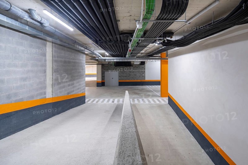 This image showcases a well-lit, modern underground parking garage with vibrant orange and white safety markings, efficient lighting, and structured piping overhead, reflecting organized urban design and functionality
