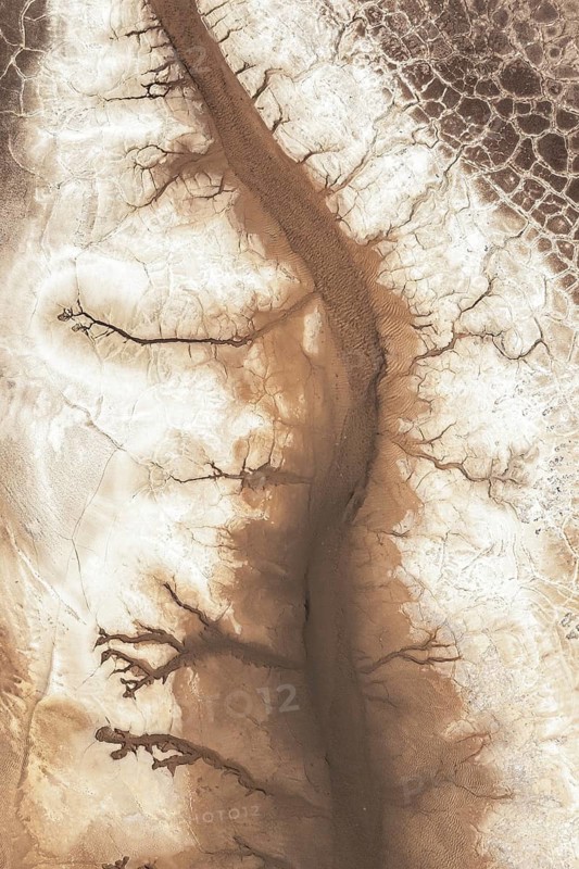 Aerial view showcasing an intricate pattern of winding cracks and textures in a desert landscape, highlighting the natural artistry and erosion of arid terrains