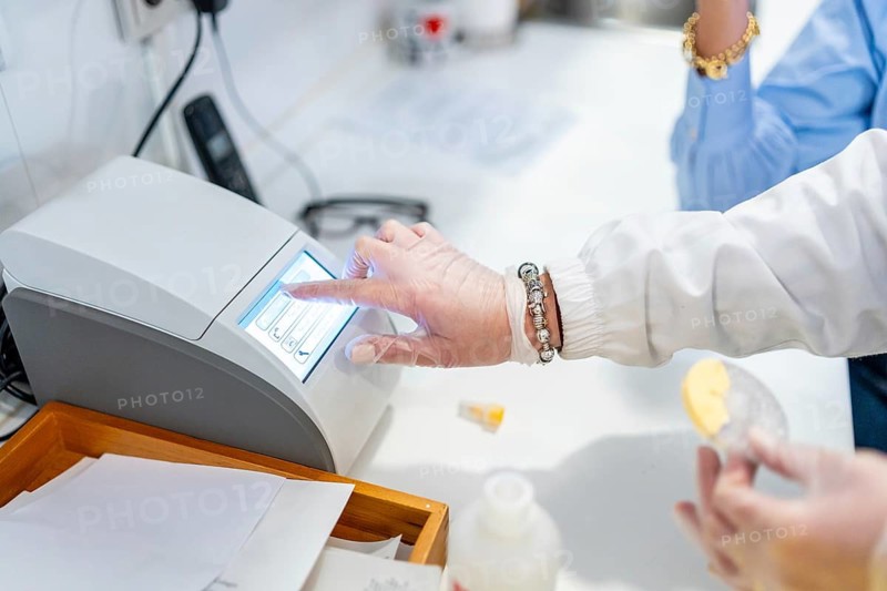 Pharmacist hand wearing protective glove interacting with a digital display on a laboratory machine, performing a medical test and preparing samples in a pharmacy or clinic setting