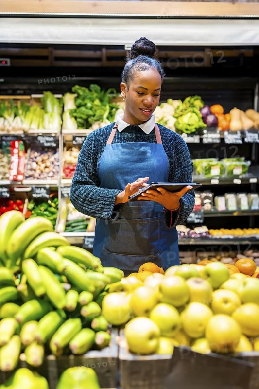 Grocery store employee managing fresh produce inventory with a digital tablet, ensuring quality and availability for customers