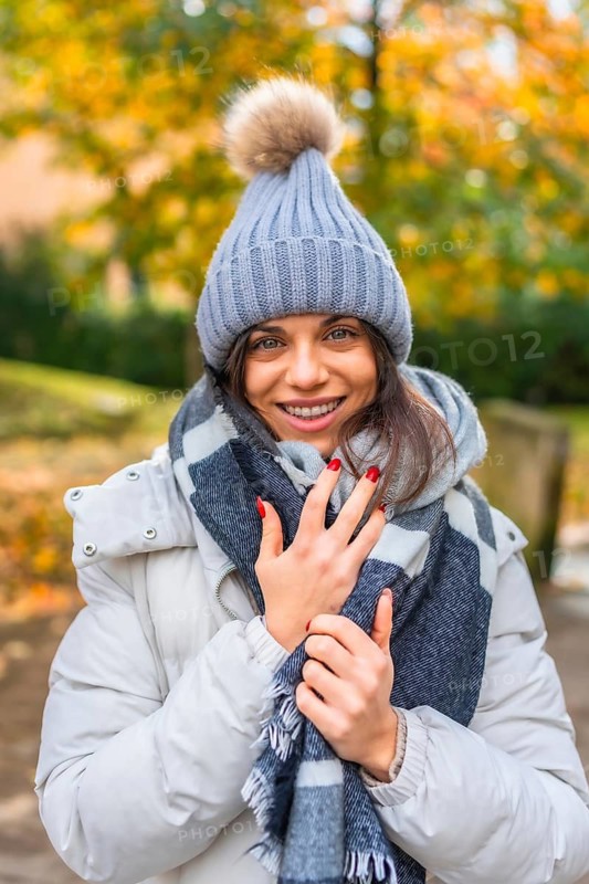 Vertical portrait of a beauty woman smiling at camera wearing warm clothes and woolly hat standing at park in autumn