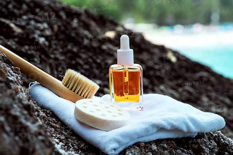 A cosmetic serum bottle enriched with vitamins and golden particles, displayed with a brush and sponge on a towel at the seaside, capturing a sense of luxury and natural skincare