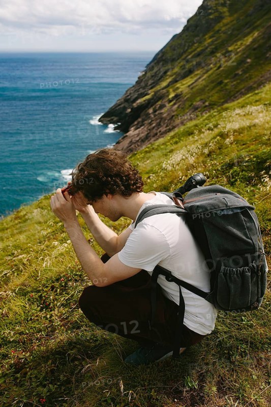 A young man at the rugged coastline of Middle Cove, Newfoundland. He is caught in a focused moment at scenic beauty of the waves crashing against the cliffs
