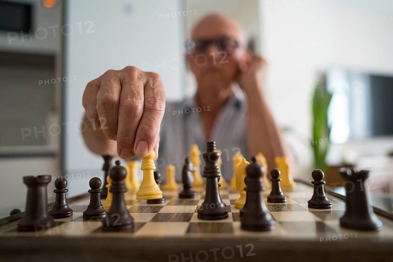 A senior man is deeply focused on a chess game at home, moving a piece thoughtfully. This intimate moment captures the joy and concentration in a beloved hobby