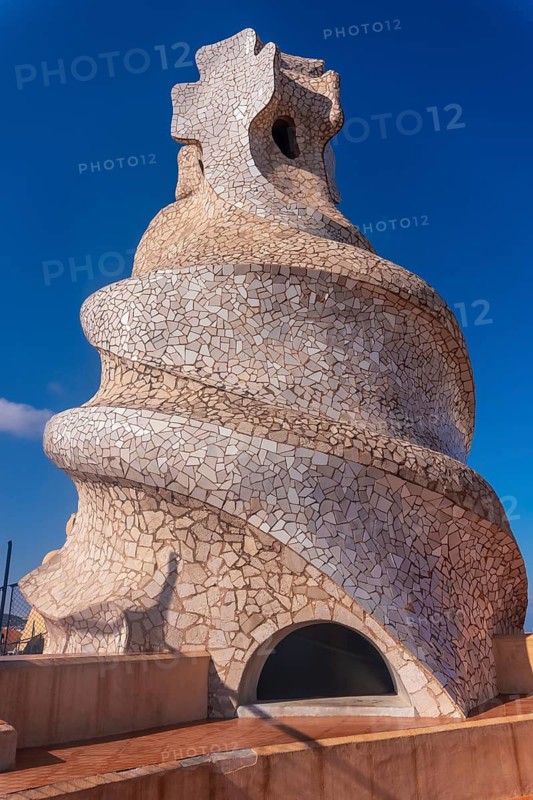 Whimsical chimney covered in colorful mosaic tiles stands out against a vibrant blue sky, showcasing the unique architecture of barcelona