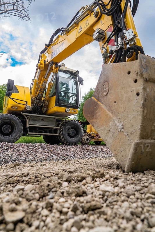 Large yellow excavator on a construction site with a shovel in the foreground and a cloudy sky in the background, track construction Hermann Hesse Bahn, Calw, Black Forest, Germany