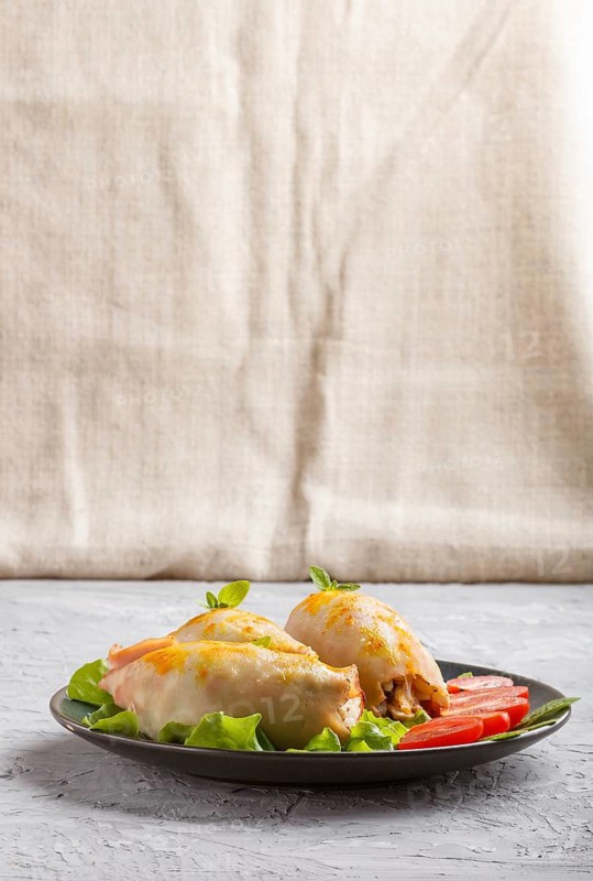 Stuffed baked squid with greens on a blue ceramic plate on a gray concrete background, side view, copy space