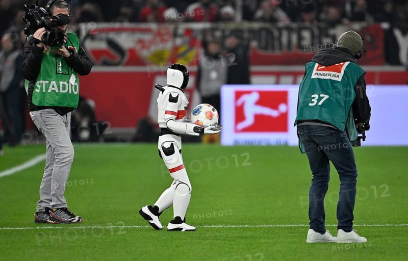 During the DFL and VfB Stuttgart Innovation Matchday, an AI-supported robot hands over the Adidas Derbystar game ball to the mascot Fritzle VfB Stuttgart logo TV camera Stuttgart soccer Bundesliga, MHPArena, MHP Arena Stuttgart, Baden-Württemberg, Germany