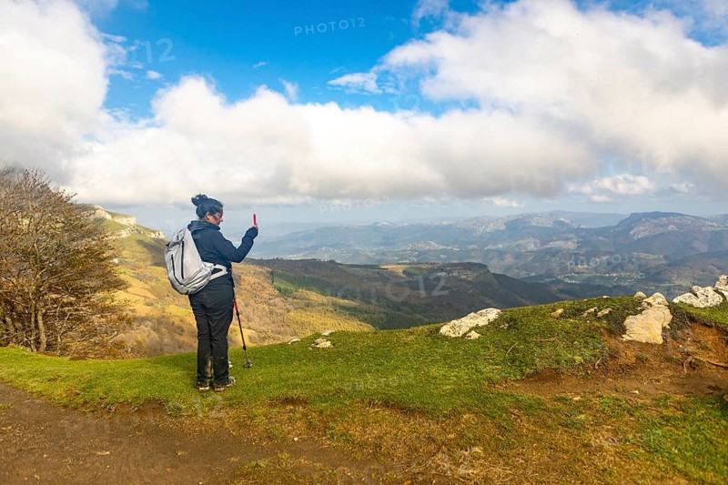 A woman hikes through the picturesque autumn landscape of Gorbea Natural Park in the Basque Country, Spain. She enjoys capturing with phone the vibrant seasonal colors and stunning views