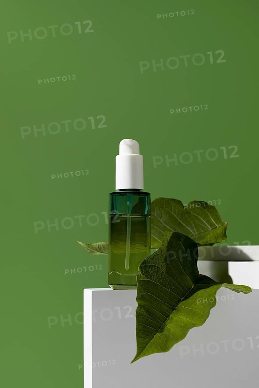 A striking image of a green essential oil bottle, adorned with a leaf, positioned on a white stand against a solid green background. This picture accentuates the natural origin and wellness theme of the product
