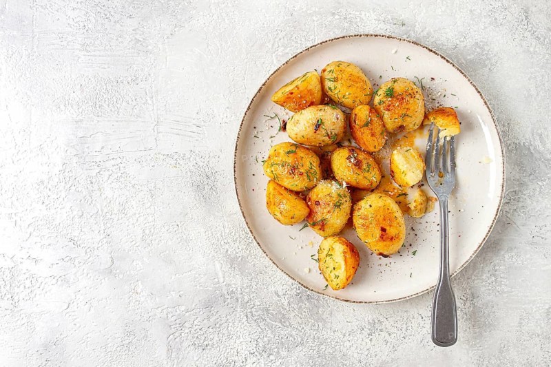 Half-eaten fried new potatoes, with butter and dill, on a white plate, with a fork, at home, no people