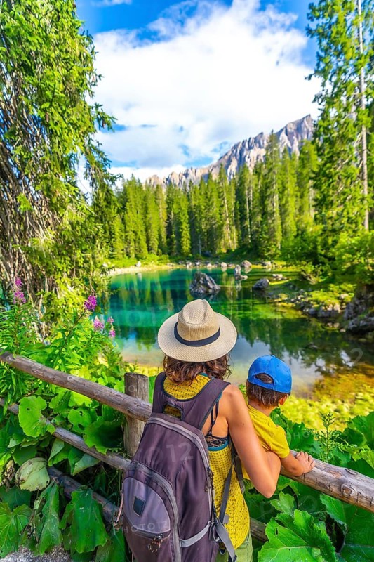 Tourists enjoying breathtaking view of lake carezza surrounded by dolomites mountains in summer