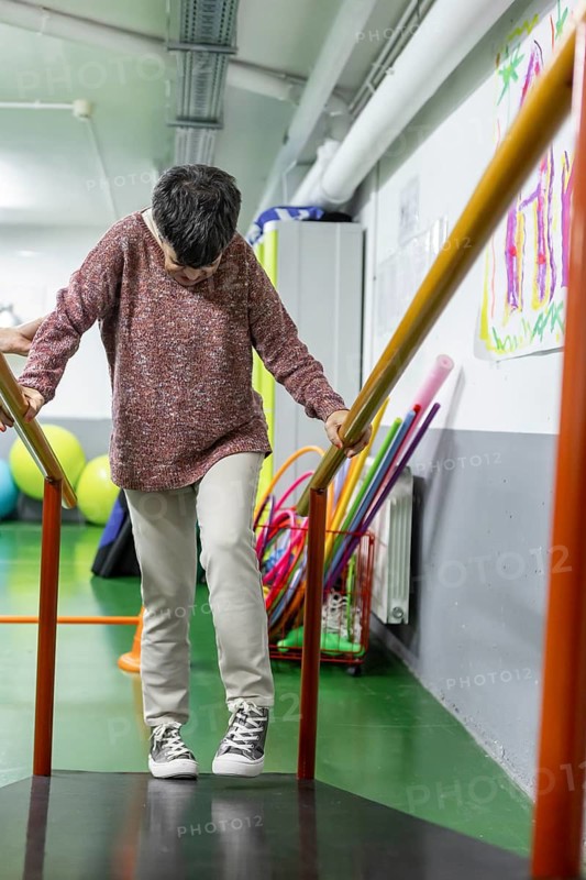 A woman steadily walks down a ramp, using handrails for support, inside a mental health residence. The scene emphasizes balance and a supportive environment