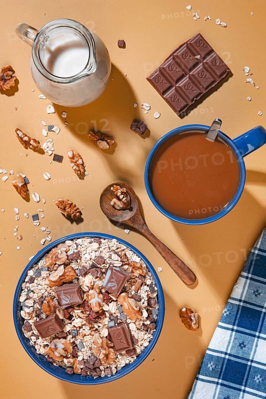 Breakfast, muesli with chocolate and walnuts next to milk and coffee from above on a yellow background