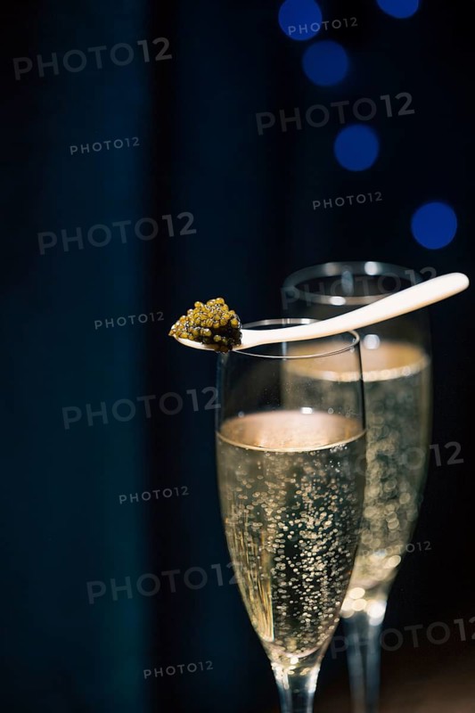 A spoonful of premium Beluga caviar presented atop a glass of bubbly champagne, set against a dark background with subtle blue lights