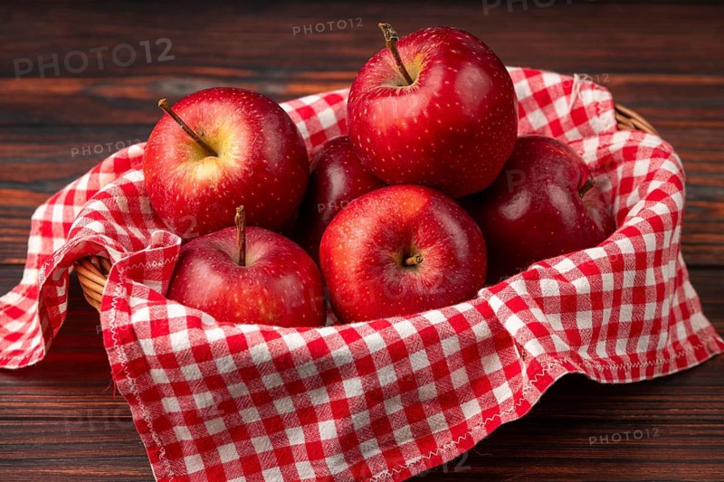 Basket with fresh, red apples on checkered cloth on a dark wooden background